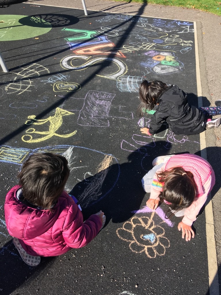 Kids drawing on the black tarmac ground with brightly coloured chalks