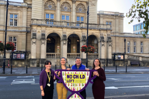 A smiling team standing in front of the town hall holding up a No Child Left Behind sign